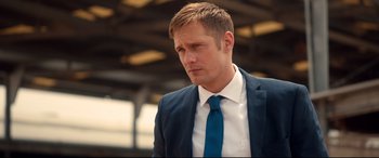Movie still from “War on Everyone” (2016), directed by John Michael McDonagh – A man in a suit and tie standing in a building; Close Up shot, Over the shoulder angle