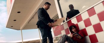 Movie still from “War on Everyone” (2016), directed by John Michael McDonagh – A man standing in front of a window holding a sign; Medium shot, Low angle