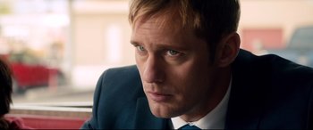Movie still from “War on Everyone” (2016), directed by John Michael McDonagh – A man in a suit and tie looking to his left; Close Up shot, Over the shoulder angle