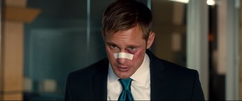 Movie still from “War on Everyone” (2016), directed by John Michael McDonagh – A person wearing a suit and tie with a bandage on his face; Close Up shot, High angle