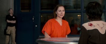 Movie still from “War on Everyone” (2016), directed by John Michael McDonagh – A woman in an orange shirt is sitting at a table; Medium shot, Over the shoulder angle