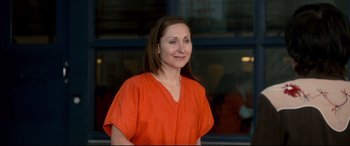 Movie still from “War on Everyone” (2016), directed by John Michael McDonagh – A woman in an orange shirt is smiling for the camera; Medium shot, Over the shoulder angle