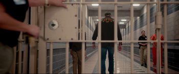 Movie still from “War on Everyone” (2016), directed by John Michael McDonagh – Two men walking in a hallway behind a jail cell; Wide shot, Over the shoulder angle