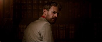 Movie still from “War on Everyone” (2016), directed by John Michael McDonagh – A man with a beard is standing in front of a book shelf; Close Up shot, Low angle