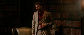 Movie still from “War on Everyone” (2016), directed by John Michael McDonagh – A man in a suit and tie standing in front of a book shelf; Medium shot, Low angle
