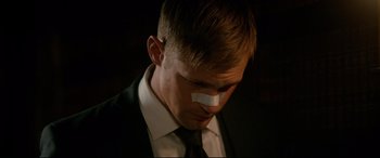 Movie still from “War on Everyone” (2016), directed by John Michael McDonagh – A man in a suit with a bandage on his face; Close Up shot, Low angle