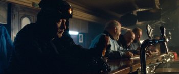 Movie still from “War, Inc.” (2008), directed by Joshua Seftel – Two men sitting at a bar with a drink in their hand; Medium shot, Low angle