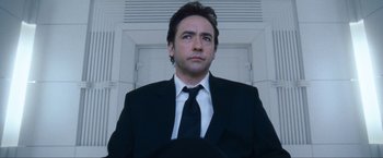 Movie still from “War, Inc.” (2008), directed by Joshua Seftel – A man in a suit and tie standing in front of a door; Close Up shot, Low angle