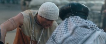 Movie still from “War, Inc.” (2008), directed by Joshua Seftel – A man wearing a white knitted hat and a black boxing glove; Close Up shot, Over the shoulder angle
