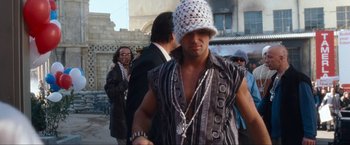 Movie still from “War, Inc.” (2008), directed by Joshua Seftel – A man wearing a white hat and a black vest; Medium shot, Low angle
