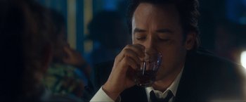 Movie still from “War, Inc.” (2008), directed by Joshua Seftel – A man in a white shirt and black tie drinking a glass of wine; Close Up shot, Over the shoulder angle