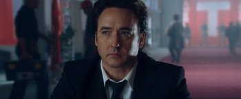 Movie still from “War, Inc.” (2008), directed by Joshua Seftel – A person wearing a suit and tie; Close Up shot, Over the shoulder angle