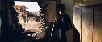 Movie still from “War, Inc.” (2008), directed by Joshua Seftel – A man in a black suit looking at his cell phone; Wide shot, Over the shoulder angle