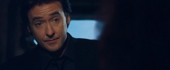 Movie still from “War, Inc.” (2008), directed by Joshua Seftel – A person wearing a suit and tie; Close Up shot, Over the shoulder angle