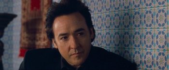 Movie still from “War, Inc.” (2008), directed by Joshua Seftel – A person wearing a suit and tie; Close Up shot, Over the shoulder angle