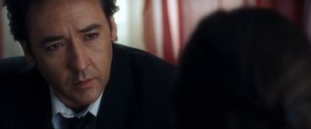 Movie still from “War, Inc.” (2008), directed by Joshua Seftel – A person wearing a suit and tie; Close Up shot, Over the shoulder angle