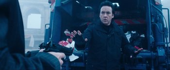 Movie still from “War, Inc.” (2008), directed by Joshua Seftel – A man holding a gun in his hand and wearing a black jacket; Close Up shot, Low angle