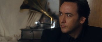 Movie still from “War, Inc.” (2008), directed by Joshua Seftel – A person wearing a suit and tie; Close Up shot, Over the shoulder angle