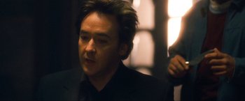 Movie still from “War, Inc.” (2008), directed by Joshua Seftel – A person wearing a suit and tie; Close Up shot, Over the shoulder angle