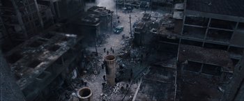 Movie still from “War, Inc.” (2008), directed by Joshua Seftel – An aerial view of a destroyed city with people walking around it; Extreme Wide shot, Overhead angle