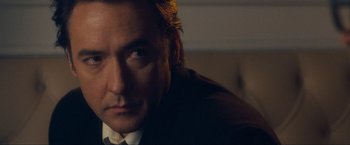 Movie still from “War, Inc.” (2008), directed by Joshua Seftel – A person wearing a suit and tie; Close Up shot, Over the shoulder angle