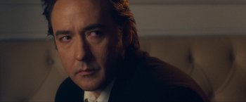 Movie still from “War, Inc.” (2008), directed by Joshua Seftel – A person wearing a suit and tie; Close Up shot, Over the shoulder angle