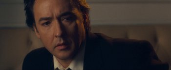 Movie still from “War, Inc.” (2008), directed by Joshua Seftel – A person wearing a suit and tie; Close Up shot, Over the shoulder angle