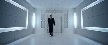 Movie still from “War, Inc.” (2008), directed by Joshua Seftel – A man in a suit and tie in a white room; Wide shot, Low angle