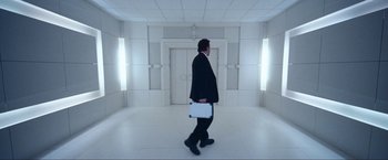 Movie still from “War, Inc.” (2008), directed by Joshua Seftel – A man in a suit is walking in a white room; Wide shot, Low angle