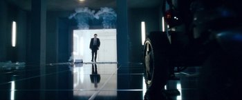 Movie still from “War, Inc.” (2008), directed by Joshua Seftel – A man in a suit and tie standing next to a car; Wide shot, Low angle
