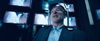 Movie still from “War, Inc.” (2008), directed by Joshua Seftel – An older man wearing a suit and tie; Close Up shot, Over the shoulder angle