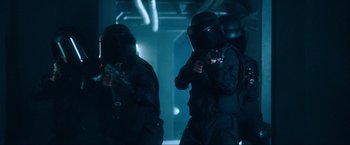 Movie still from “War, Inc.” (2008), directed by Joshua Seftel – A group of men in black suits and helmets; Medium shot, Low angle