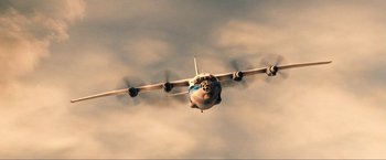Movie still from “War, Inc.” (2008), directed by Joshua Seftel – An airplane is flying through the air in a cloudy sky; Extreme Wide shot, Low angle