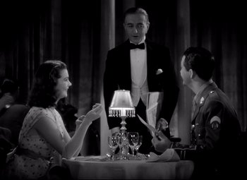 Movie still from “Waterloo Bridge” (1940), directed by Mervyn LeRoy – A man standing at a table with two women; Medium shot, Low angle