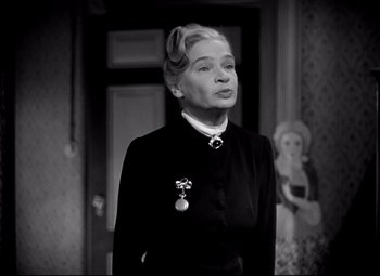 Movie still from “Waterloo Bridge” (1940), directed by Mervyn LeRoy – An older woman wearing a black suit and a medal; Medium shot, Low angle