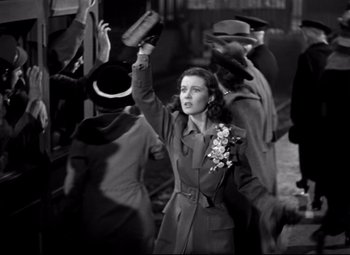 Movie still from “Waterloo Bridge” (1940), directed by Mervyn LeRoy – A woman in a trench coat holding her arm up; Medium shot, Low angle