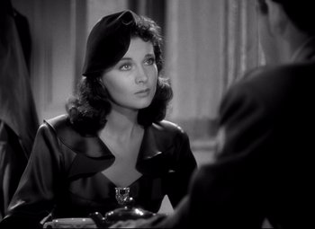 Movie still from “Waterloo Bridge” (1940), directed by Mervyn LeRoy – A woman sitting at a table with a glass of wine; Close Up shot, Over the shoulder angle