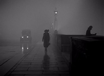 Movie still from “Waterloo Bridge” (1940), directed by Mervyn LeRoy – A person walking down a sidewalk in the fog; Wide shot, Low angle
