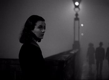 Movie still from “Waterloo Bridge” (1940), directed by Mervyn LeRoy – A black and white photo of a woman standing in front of a street light; Medium shot, Over the shoulder angle