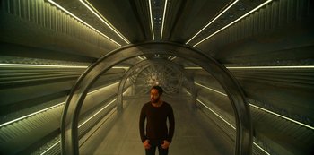 Movie still from “Another Life” (2019), created by Aaron Martin – A man standing inside of a tunnel with lights on; Wide shot, High angle