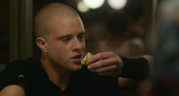 Movie still from “We Are Your Friends” (2015), directed by Max Joseph – A man eating a piece of food while sitting down; Close Up shot, Over the shoulder angle
