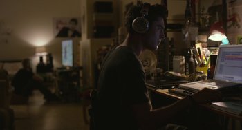 Movie still from “We Are Your Friends” (2015), directed by Max Joseph – A young man wearing headphones is sitting at a computer desk; Medium shot, Over the shoulder angle