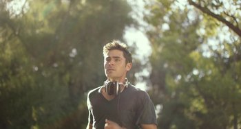 Movie still from “We Are Your Friends” (2015), directed by Max Joseph – A young man wearing headphones while standing in a park; Medium shot, Low angle