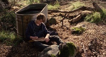 Movie still from “We Bought a Zoo” (2011), directed by Cameron Crowe – A young man sitting on the ground writing on a piece of paper; Wide shot, High angle