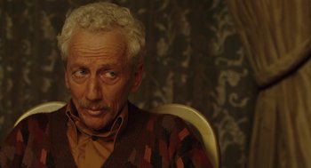 Movie still from “We Own the Night” (2007), directed by James Gray – An older man sitting in a chair looking at the camera; Close Up shot, Low angle
