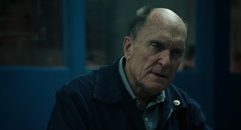 Movie still from “We Own the Night” (2007), directed by James Gray – An old man with a bald head is sitting down; Close Up shot, Over the shoulder angle