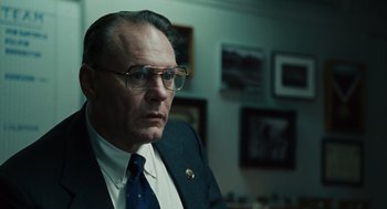 Movie still from “We Own the Night” (2007), directed by James Gray – An older man wearing glasses and a suit and tie; Close Up shot, Low angle