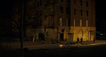 Movie still from “We Own the Night” (2007), directed by James Gray – A car parked on the side of the street at night; Extreme Wide shot, Low angle
