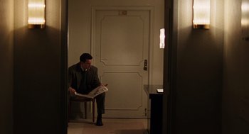 Movie still from “We Own the Night” (2007), directed by James Gray – A man sitting in a chair reading a newspaper; Wide shot, Low angle