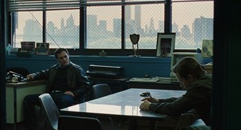 Movie still from “We Own the Night” (2007), directed by James Gray – Two people sitting at a table in front of a city skyline; Wide shot, Over the shoulder angle
